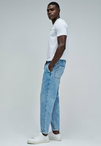 Camiseta blanca de manga corta combinada con jeans de mezclilla azul claro y zapatillas blancas. Los jeans tienen un bolsillo lateral y un corte relajado.