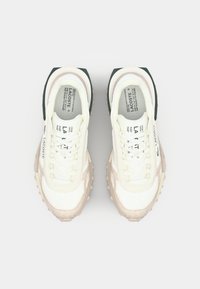 Lacoste sneakers met een crèmekleurige bovenkant, beige accenten en zwarte hieldetails. Voorzien van een gestructureerde zool en witte veters.