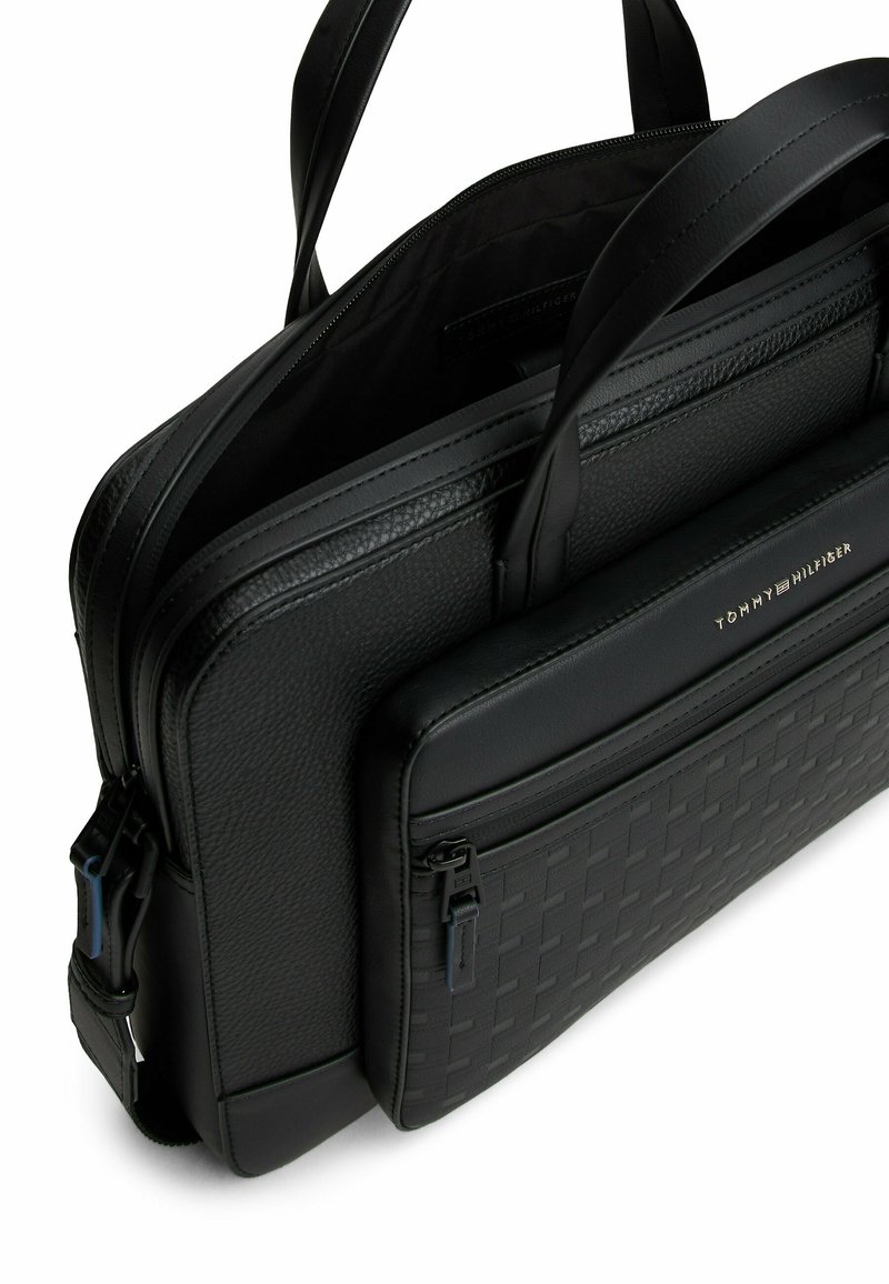 Black leather briefcase with a textured design, dual zippers, and two handles. Features a front pocket with a smooth finish and subtle branding.