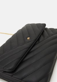 Borsa in pelle nera trapuntata con logo dorato, dotata di un pattina pieghevole e una tracolla in catena dorata. Tessuto liscio con cuciture verticali.