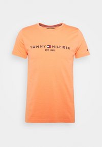 Camiseta de algodón naranja con cuello redondo y mangas cortas, que presenta el texto y el logotipo en negro de "TOMMY HILFIGER", y un sutil acento en rojo y azul en el cuello.