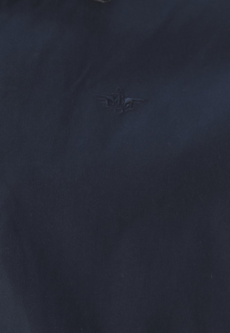 Tessuto blu navy dalla consistenza liscia, con un logo in rilievo di un'ancora aliata sul lato sinistro. Leggero lucido visibile.