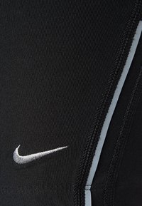 Sorte sportlige leggings med en glat tekstur, kontrastfarvet hvid syning og et sølvfarvet Nike-logo nær taljen.