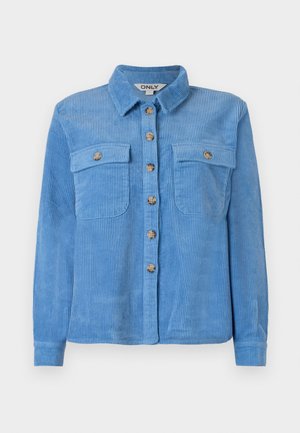 Svetlomodrá kordová košeľa s dlhými rukávmi, predným zapínaním na gombíky, dvoma náprsníkovými vreckami a špicatým golierom. Obsahuje hnedé gombíky.