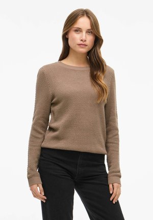 Pull en laine texturé marron clair avec un col rond et des manches longues, associé à un pantalon noir. Le tissu présente un motif tissé distinct.