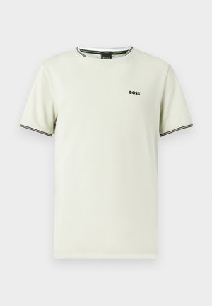 Īsām piedurknēm krekls no gaiši bēša kokvilnas, ar apaļu kaklu, melnu logotipu un kontrastējošām melnām un baltām svītrām apkaklī un piedurknēs.