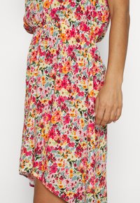 Vestido floral com uma mistura de flores rosas, laranjas e amarelas sobre um fundo claro, feito de tecido leve e com um corte descontraído.