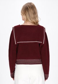 Maglione bordeaux con colletto largo, texture a coste e dettagli a righe bianche all'orlo e ai polsini, pensato per una vestibilità ampia.