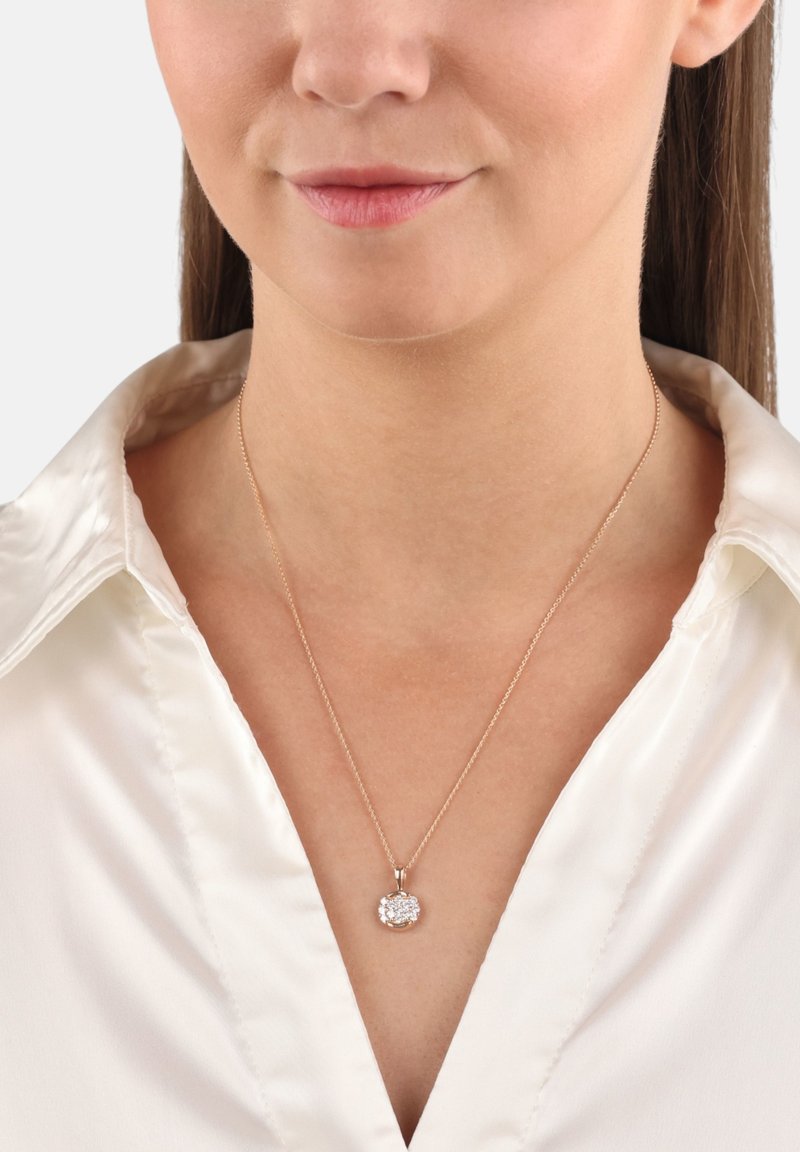 Collana in oro rosa con pendente circolare che presenta un mazzo di gemme bianche. La catena è delicata e si abbina a una blusa bianca in satin.