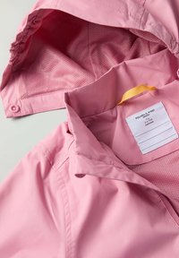 Vaaleanpunainen vedenpitävä takki, jossa on verkkovuori, napit ja keltainen ripustuslenkki. Sisäkauluksessa on etiketti.