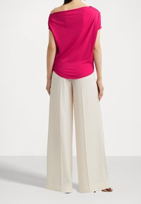 Fuchsian av axelblus i kombination med krämfärgade vida byxor. Mjuk tygkvalitet med avslappnad passform och rundad nederkant.