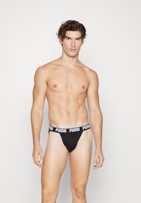 Schwarze Tangas mit einem breiten weißen Puma-Logo-Bund, hergestellt aus einem glatten Stoff und in figurschmeichelnder Passform.