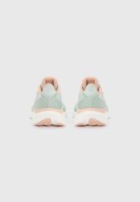 Ζευγάρι αθλητικών παπουτσιών σε ανοιχτό πράσινο και ροδάκινο, εμφανιζόμενα από πίσω, σε απλό ανοιχτό γκρι φόντο.