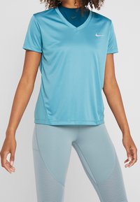 Ljusblå atletisk damtröja med V-halsdesign och korta ärmar, tillverkad av ett mjukt, andningsbart tyg. Noterbar Nike-logotyp på bröstet.