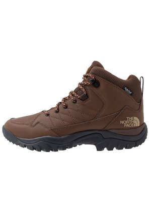 Bruine North Face wandelschoen met middenhoogte, zwarte zool, gewatteerde kraag, vetersluiting en HydroSeal waterdichte label aan de zijkant.