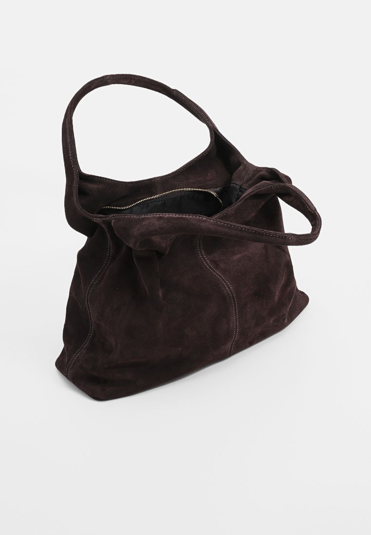 Bolso tote de ante en marrón oscuro. Presenta una textura suave, dos asas largas y un cierre de cremallera. Forma redondeada con detalles de costura.