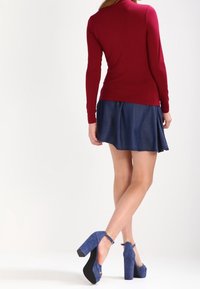 Pitkähihaista marjapunaista paitaa on yhdistetty farkkuhameeseen. Mallilla on päällään siniset mokkasiinit, joissa on nilkkaketjut ja paksu korko.