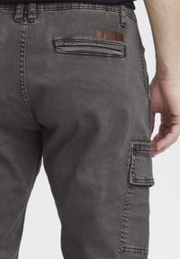 Gray denim cargo pants featuring a side pocket, a back pocket with a leather label, and a textured finish.