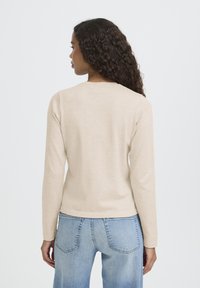 Bež dolgotrajna majica z dolgimi rokavi in okrolim izrezom, gladke teksture in oprijetega kroja, kombinirana s svetlo modrimi visokim pasom kavbojkami.