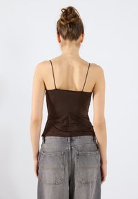 Bruine aansluitende cami met dunne banden, met een zachte textuur. Gecombineerd met hoge, losse grijze denim jeans.