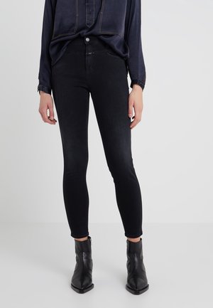 Jean noir slim associé à des bottines noires et une chemise longue à manches longues bleu marine avec des détails de couture apparents.