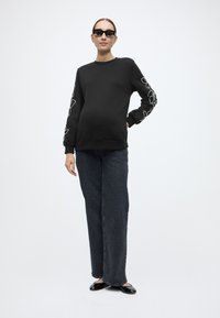 Μαύρο φούτερ με λευκά λουλουδένια σχέδια στα μανίκια, σε συνδυασμό με σκούρο τζιν παντελόνι φαρδιάς γραμμής και μαύρες μπαλαρίνες. Λείο ύφασμα, άνετη εφαρμογή.