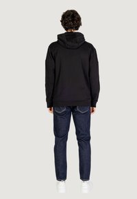 Felpa nera con cappuccio, dalla vestibilità comoda, abbinata a jeans blu scuro. L'outfit presenta una texture liscia e un design minimalista.