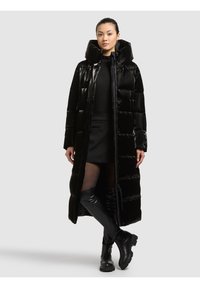 Melnas pūkains jaka ar augstu apkakli, spīdīgu apdari un horizontālu rievotu rakstu. Valkāta virs cieši pieguloša melna apģērba un melnu zābaku līdz ceļiem.