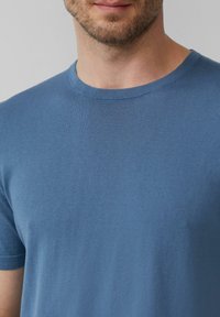 Koszulka z okrągłym dekoltem wykonana z miękkiej, tkanej niebieskiej tkaniny o gładkiej strukturze. Posiada krótkie rękawy i prosty, klasyczny fason.