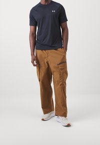 Tmavě šedé sportovní tričko s krátkým rukávem; hnědé cargo kalhoty s bočními kapsami a šedými zipy; světle šedé tenisky s oranžovými detaily.