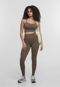 Brown activewear set consisting of a cropped tank top and high-waisted leggings, paired with a light-colored shoulder bag and sneakers.