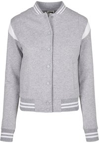 Veste universitaire gris clair avec boutons-pression, rayures blanches sur le col, les poignets et la ceinture, et accents blancs sur les manches.