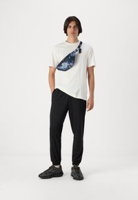 Hvid t-shirt med korte ærmer, sorte joggers og sorte sneakers. Blå og hvid tie-dye crossbody taske på skulderen. Simpel design, afslappet pasform.