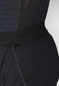 Zwarte sportieve bodysuit met textuurstof, mesh-panelen, een elastische tailleband en contrasterende stikdetails.
