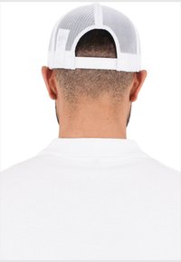 Gorra blanca de malla con correa ajustable en la parte posterior, que presenta un visor sólido y un copete redondo que revela el cabello corto.
