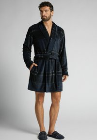 Marinblå rutmönstrad badrock i mjukt tyg med långa ärmar, sjalkrage och knytband i midjan. Har två framfickor och är knälång.