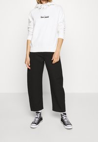 Sudadera blanca con "Lee Jeans" bordado en negro en la parte frontal, combinada con pantalones negros holgados y zapatillas altas negras.