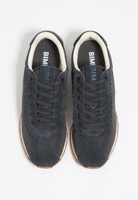 Zapatillas gris oscuro que combinan materiales de ante y textil, con un diseño texturizado, acentos en forma de onda y cordones oscuros.