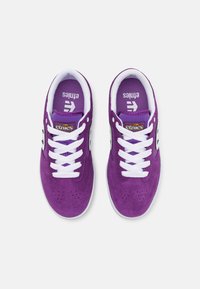 Μωβ σουέτ αθλητικά παπούτσια με λευκές δέστρες και ραφές. Διαθέτουν περφορέ το κουτί του ποδιού και μαύρες λεπτομέρειες. Λογότυπο Etnies στη γλώσσα.