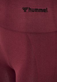 Bordeauxfarbene Sportleggings aus strukturiertem Material, mit einem schwarzen "hummel"-Logo am Bund und vertikalen Rippdetails.