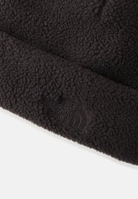 Fekete bolyhos sapka, textúrált felülettel, a "The North Face" diszkrét, dombornyomott logójával az elülső részen.