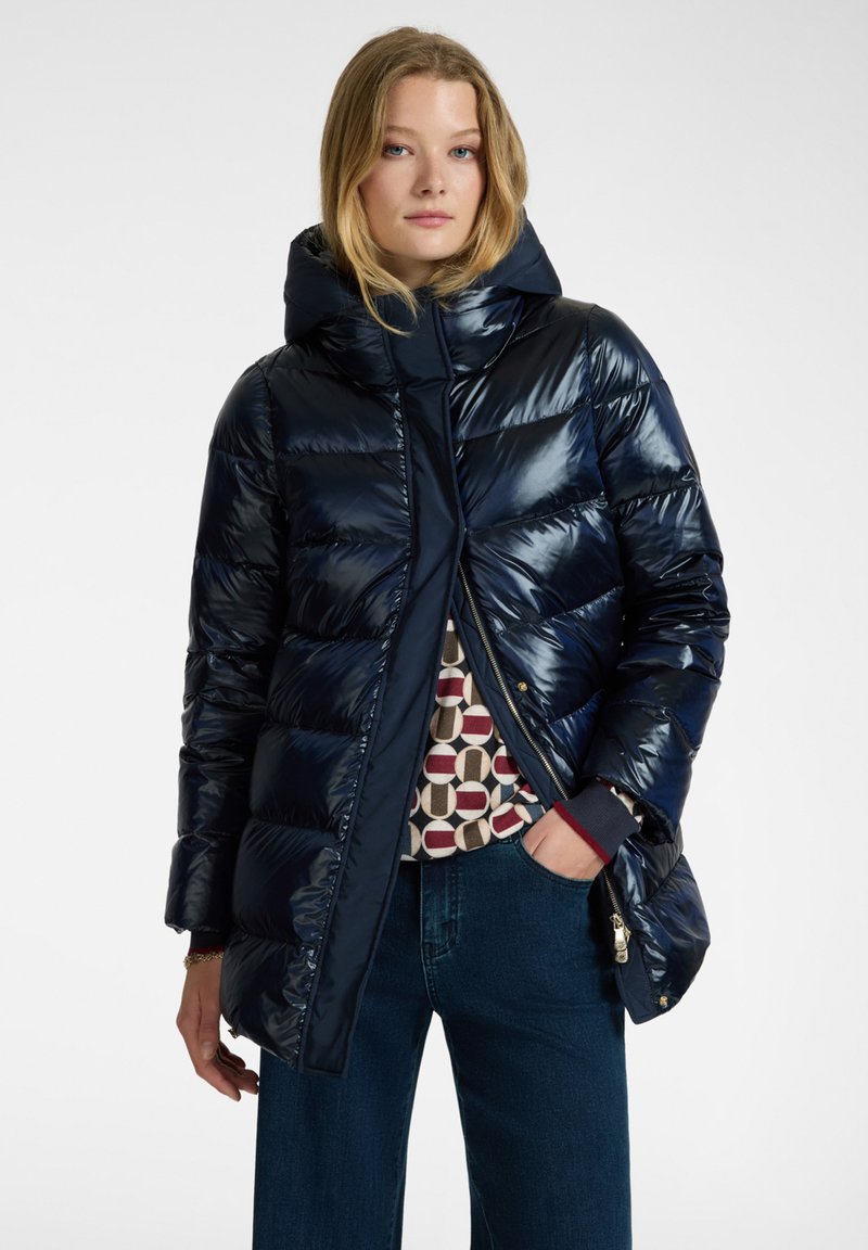 Giacca a vento blu navy con finitura lucida, cappuccio e design patchwork sotto. Presenta una chiusura con zip e tasche laterali.