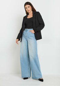 Blazer noir sur un haut noir, associé à un jean large taille haute bleu clair. Coupe slim avec une texture lisse et des détails de poches subtils.