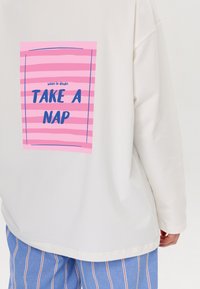 Weiße Sweatshirt mit einem pink gestreiften Grafik auf der Rückseite und dem Text "when in doubt TAKE A NAP" in Blau. Weicher Stoff, lässige Passform.