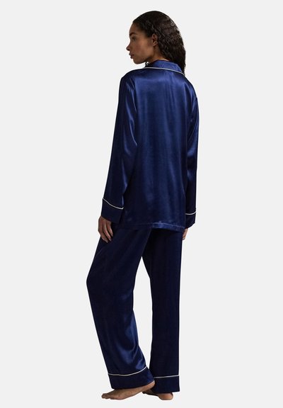 Marineblauwe satijnen pyjama met een top met lange mouwen en witte bies, en loszittende broek met contrasterende bies aan de boorden.