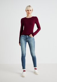 Langermet burgunder topp, tettsittende design, med rund hals. Kombinert med lyseblå slitte skinny jeans og hvite sneakers med røde detaljer.