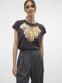 Un t-shirt gris foncé présente un design graphique de plume dorée, des manches courtes et une coupe décontractée. Le modèle l'associe avec un pantalon taille haute gris.