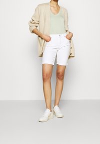 Bílé denimové kraťasy spárované se světle zeleným topem a béžovým pleteným cardiganem. Bílé tenisky s detaily. Neformální oblečení s volným střihem.