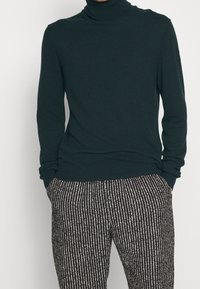 Mörkgrön polotröja i mjukt stickat material, kombinerad med svart och vitrandiga byxor med avslappnad passform och ribbade muddar.