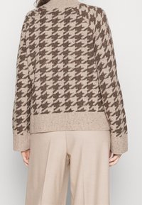 Strickpullover mit Hahnentrittmuster in Beige und Braun, mit hohem Kragen, geripptem Saum und lockerer Passform.